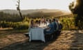 Diners eating on a long table outdoors in a field at sunset