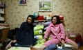 Mother and adult daughter sit on a bed, with childhood toys visible