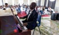 An African man in a bow tie and suit sits at a grand piano with his eyes closed as an audience listens