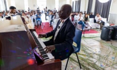 An African man in a bow tie and suit sits at a grand piano with his eyes closed as an audience listens