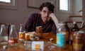 A man sitting at a dining table, looking dejected and tired, surrounded by empty bottles of ginger beer.