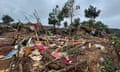 People walk amid wood and other debris strewn across the ground next to some collapsed huts