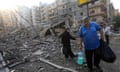 A man and woman carry belongings amid the rubble of damaged buildings