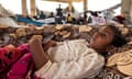 A young child partly covered with a blanket gazes upwards in a displacement camp