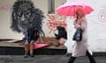 A woman walks past two people sitting on a bench, one under blankets