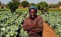 A smiling South African woman stands before a field of cabbages and other crops