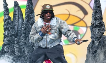 A young black African man wearing sunglasses and a cap performs on stage