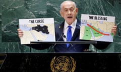 Benjamin Netanyahu, wearing a blue suit and tie, speaks at a podium as he holds two maps labeled 'The Curse' and 'The Blessing'