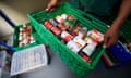 A food bank worker carries a basket of tinned tomatoes