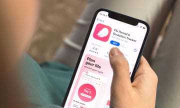 A woman's hand holding a smartphone and looking at a period and ovulation tracker