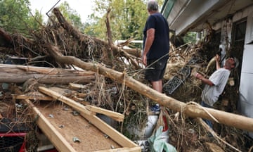 two men stand and look at fallen tree and debris in front yard