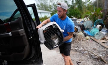 Man in ball cap loads cat in hard plastic carrier into front of pickup truck.