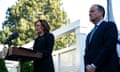 a woman speaks at a podium as a man looks on